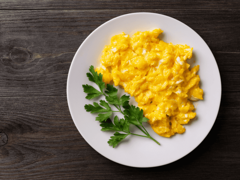 Clotted Cream Scrambled Eggs on a white plate with green herbs on top