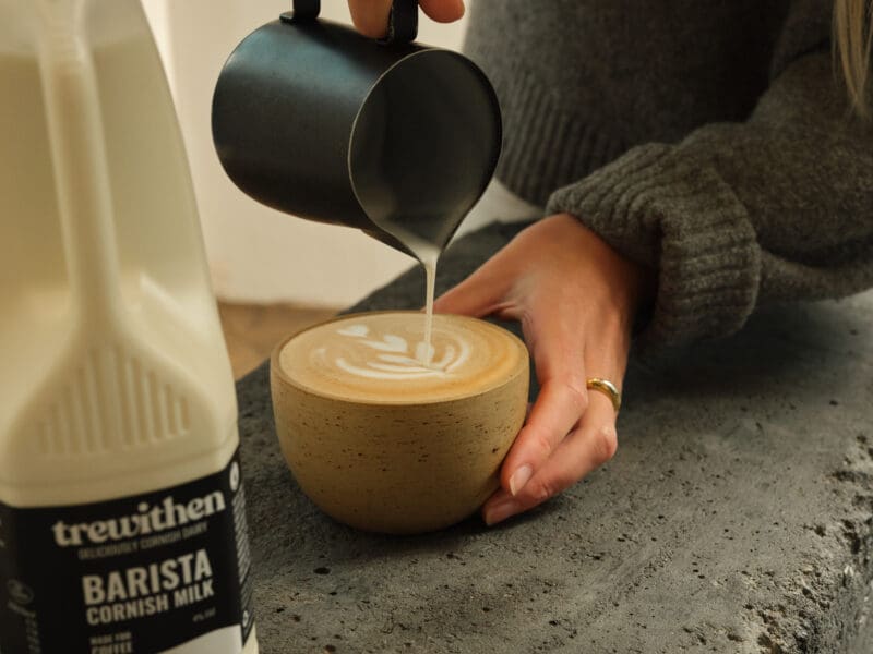 person pouring Trewithen barista milk into a cup of coffee