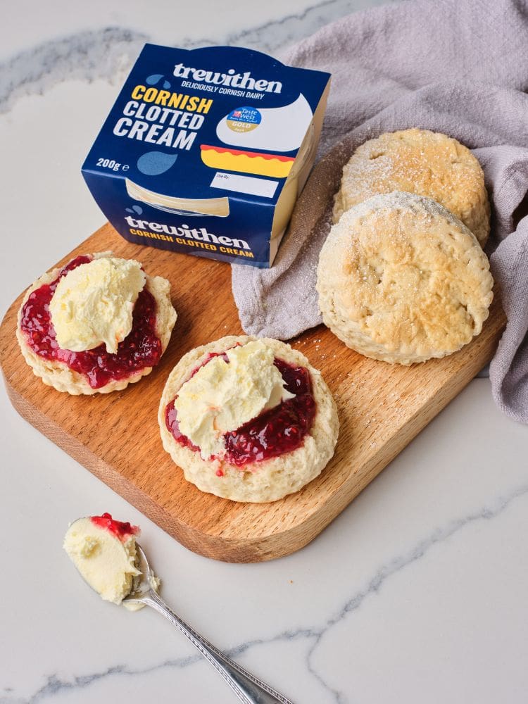 A wooden board with four scones, two with jam and clotted cream and a pot of Trewithen clotted Cream.